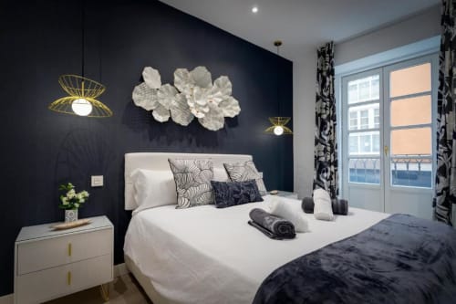 Dormitorio moderno en Spacio Menina, Burgos - pared de acento oscuro, cama blanca, flores decorativas, iluminación dorada, balcón