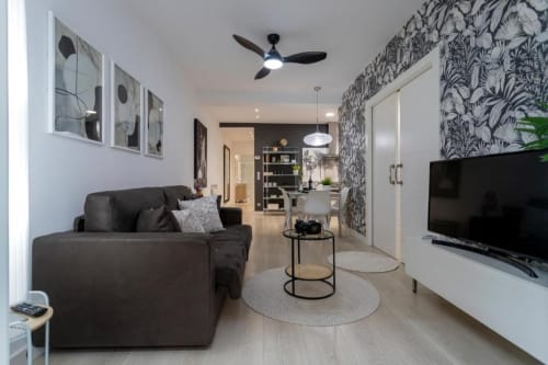 Sala de estar moderna del apartamento Spacio Menina en Burgos con sofá negro, papel pintado estampado, TV y cocina abierta