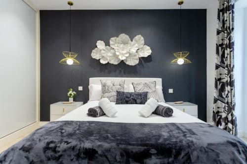 Dormitorio moderno en Spacio Menina de Burgos con pared de acento oscuro, cama blanca, lámparas colgantes doradas y arte floral decorativo
