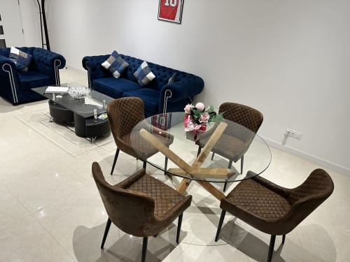 Espace de restauration et séjour moderne aux Gîtes Les Camélias 71 avec table ronde en verre, chaises matelassées marron et canapé bleu marine