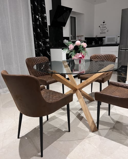 Salle à manger moderne aux Gîtes Les Camelias 71 avec table en verre, base en bois, chaises en cuir marron et composition florale rose