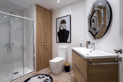 Baño moderno del apartamento Audrey en Burgos con tocador de madera, ducha, inodoro y cuadro de Audrey Hepburn