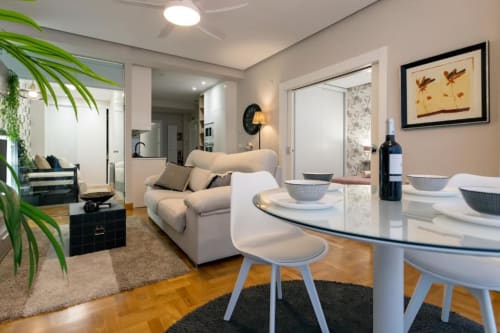 Moderna sala de estar en Burgos con mesa de comedor, sofá blanco, cocina y vistas a la ciudad en Unique Rooms
