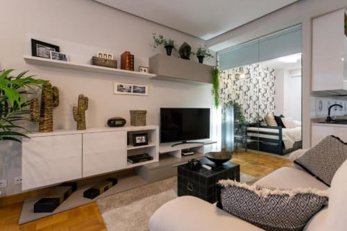 Apartamento Audrey en Burgos con sala de estar moderna, TV, muebles blancos, plantas y cocina abierta integrada con dormitorio
