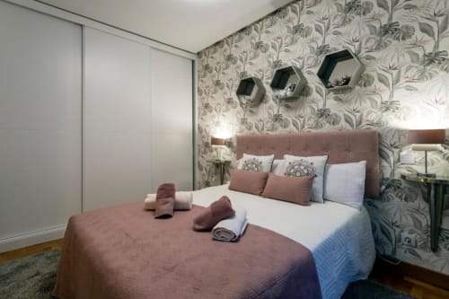 Dormitorio elegante en apartamento Audrey de Unique Rooms, Burgos, con papel pintado botánico, cabecero malva y comodidades modernas