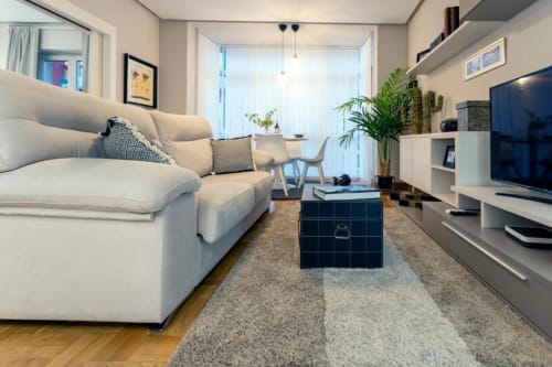 Elegante salón en Audrey by Unique Rooms, Burgos, con sofá crema, TV, plantas y vistas a la ciudad desde el balcón
