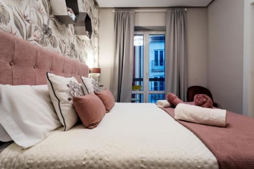 Habitación moderna en Audrey Unique Rooms de Burgos con cabecero rosa palo, ropa de cama blanca y vistas a la ciudad desde el balcón