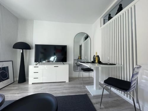 Moderna sala de estar con muebles blancos, televisor de pantalla plana, espejo de tocador y detalles en negro en hotel de Burgos