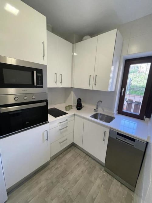 Moderna cocina blanca en apartamento Urban Home, Burgos con electrodomésticos de acero inoxidable y piso de madera