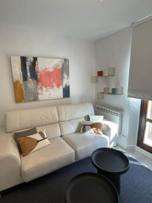Sala de estar moderna en apartamento Urban Home, Burgos con sofá crema, obra de arte abstracto, estanterías y mobiliario contemporáneo