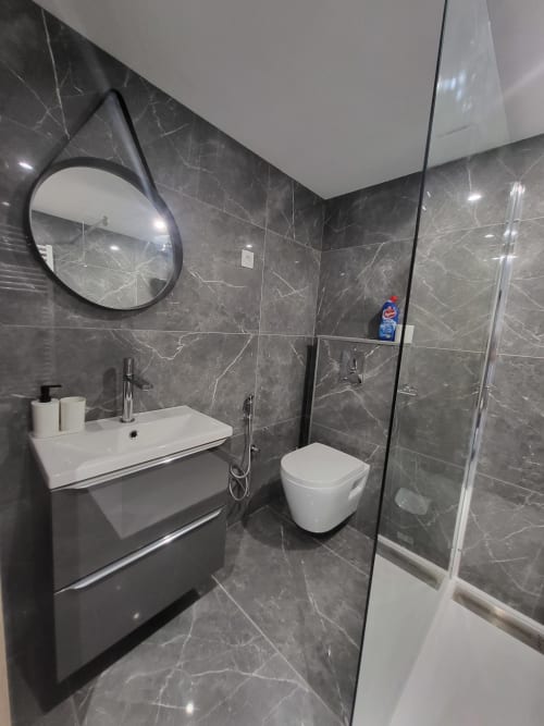Salle de bains moderne aux Gîtes Les Camélias 71 avec carrelage en marbre noir, lavabo blanc, toilettes et douche à l'italienne