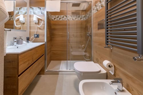 Bagno moderno nella Cricket Room di Macramè Fazello, Sciacca con finiture in legno, doccia in vetro, bidet e scaldasalviette