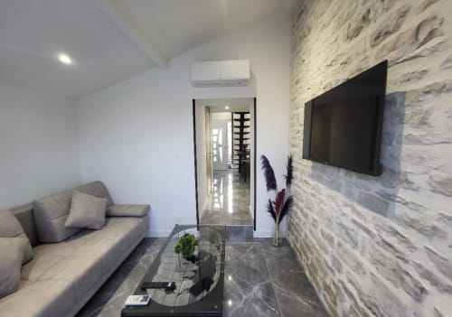 Séjour moderne aux Gites Les Camelias à Oslon avec canapé gris, télévision écran plat, mur en pierre et accès au jardin