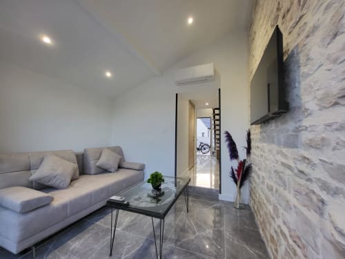 Salon moderne aux Gîtes Les Camélias 71 à Oslon avec canapé gris, mur en pierre et mobilier épuré