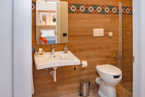 Bagno moderno nella Stanza Insolia di Macramè Fazello, Sciacca con pareti in legno, lavabo bianco, toilette e doccia accessibile.