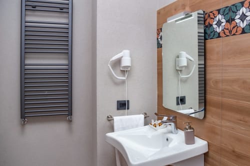 Bagno moderno di Macramè Fazello a Sciacca con lavabo bianco, specchio illuminato, scaldasalviette e pareti rivestite in legno.