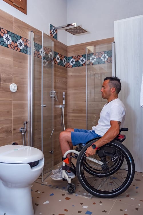 Bagno accessibile nella Stanza Insolia di Macramè Fazello, Sciacca - utente in sedia a rotelle nella zona doccia con maniglie di sicurezza