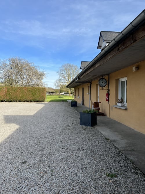 Façade du gîte Le Clos De La Vallée à Bellengreville avec allée gravillonnée, murs jaunes, horloge et jardins verdoyants