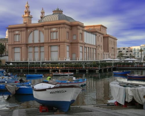 Vista sul waterfront di Finella Charming Rooms a Bari con barche da pesca e affascinante edificio storico rosa