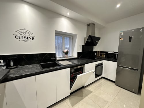 Cuisine moderne aux Gîtes Les Camelias 71 à Oslon avec armoires blanches, plan de travail en marbre noir et acier inoxydable