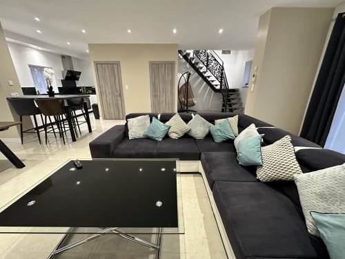 Séjour moderne avec canapé sectionnel noir, salle à manger et escalier aux Gîtes Les Camélias 71 à Oslon