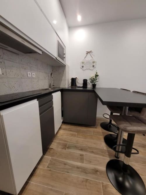 Cuisine moderne avec plans de travail noirs, armoires blanches et coin bar à l'Appart Hôtel Panambi à Chevilly-Larue