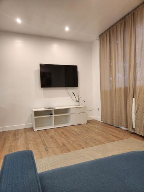 Salon moderne de l'Appart Hôtel Panambi avec TV murale, rangement blanc, parquet et teintes beige