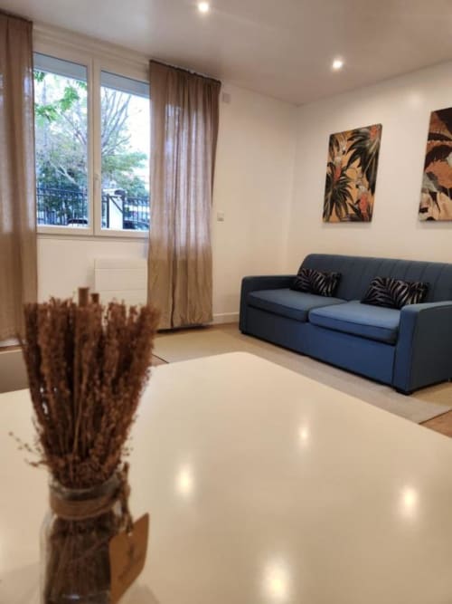 Salon moderne de l'Appart Hôtel Panambi avec canapé bleu, grandes fenêtres sur Chevilly-Larue