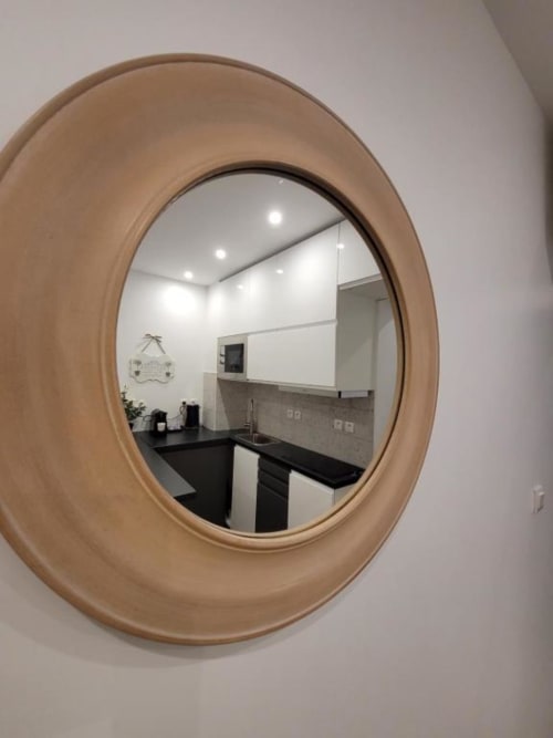 Miroir ovale à cadre bois reflétant la cuisine moderne aux comptoirs noirs d'Appart Hôtel Panambi, Chevilly-Larue