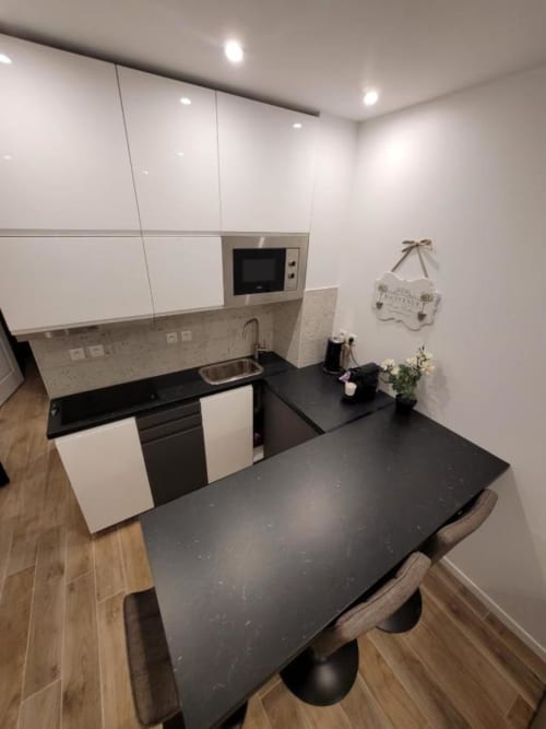 Cuisine-salle à manger moderne à l'Appart Hôtel Panambi avec plans de travail noirs, mobilier blanc et table de repas