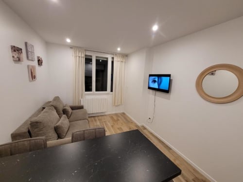 Séjour moderne de l'Appart Hôtel Panambi avec canapé beige, télévision, parquet et vue sur la ville à Chevilly-Larue