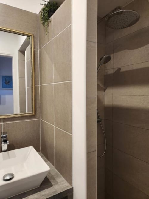 Salle de bain moderne à l'Appart Hôtel Panambi avec douchette pluie, lavabo blanc et carrelage neutre