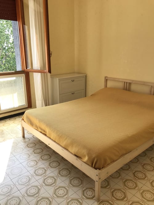 Camera luminosa in Rigiariloo Home Apartments con pareti gialle, letto in legno, cassettone e vista sul giardino dalla finestra aperta