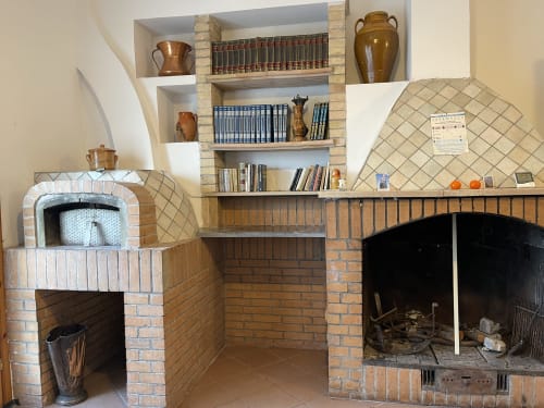 Rustico camino in mattoni e forno a legna con scaffali contenenti libri e ceramiche agli Appartamenti Rigiariloo Home