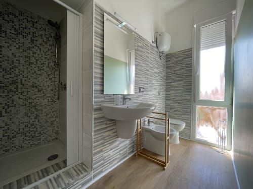 Bagno moderno presso gli Appartamenti Rigiariloo con doccia a mosaico, lavabo su colonna, WC e porta in vetro