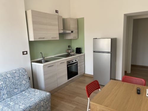 Moderna zona cucina-soggiorno di Rigiariloo Home Apartments con elettrodomestici in acciaio inox, schienale verde, tavolo in legno