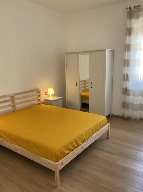 Camera luminosa presso Rigiariloo Home Apartments con biancheria gialla, letto in legno, armadio e tende a righe a San