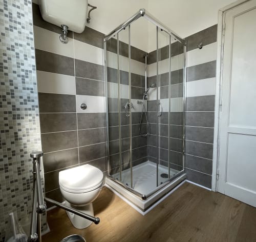 Bagno moderno di Rigiariloo Home Apartments con piastrelle a righe, doccia in vetro e pavimento in legno