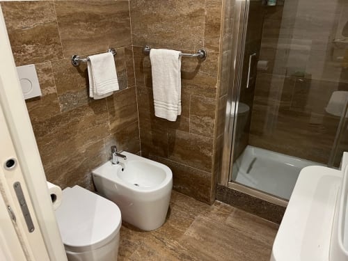 Bagno moderno della Michelangelo Suite Roma con piastrelle marroni, sanitari bianchi, portasciugamani e box doccia in vetro