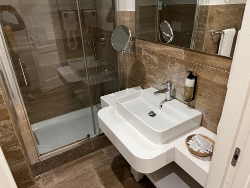 Bagno moderno in hotel a Roma con doppio lavabo, doccia in vetro, rivestimenti in piastrelle marroni e finiture contemporanee