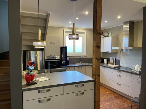 Cuisine moderne avec meubles blancs, suspensions, poutre bois et sculpture de pomme rouge aux Gîtes Boulogne Sur