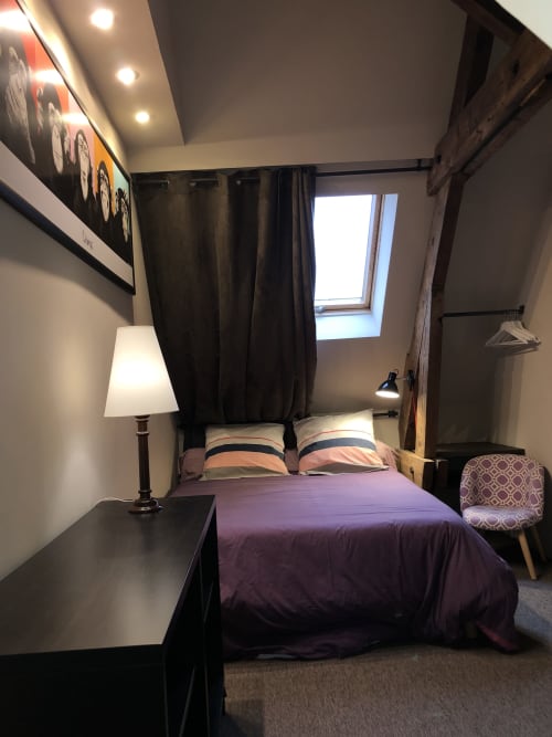 Chambre cozy du gîte Boulogne Sur Mer avec literie mauve, rideaux noirs, fenêtre de toit, lampe de bureau et chaise