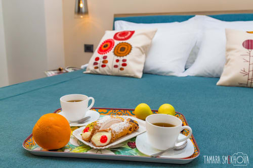 Vassoio colazione con caffè, pasticcino, arancia e limoni sul letto presso le camere Macramè Fazello a Sciacca
