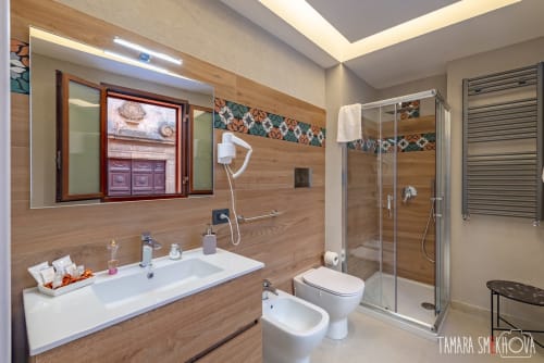 Bagno moderno nella Camera Perricone di Macramè Fazello B&B, Sciacca con pareti in legno, doppio lavabo, doccia in vetro e