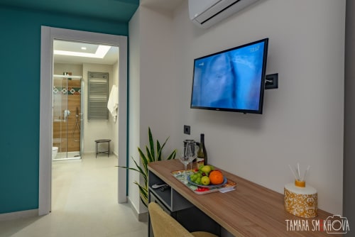 Camera moderna al Macramè Fazello di Sciacca con TV, scrivania in legno, frutta fresca, pianta e bagno