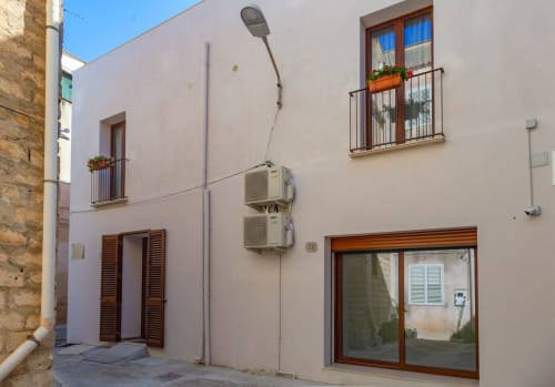 Facciata bianca di casa mediterranea con finiture in terracotta, finestre con condizionatori e fioriere a Sciacca, Sicilia