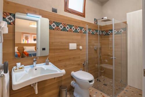 Bagno moderno nella Insolia Room di Macramè Fazello, Sciacca con rivestimenti in legno, lavabo, WC e doccia con box in vetro