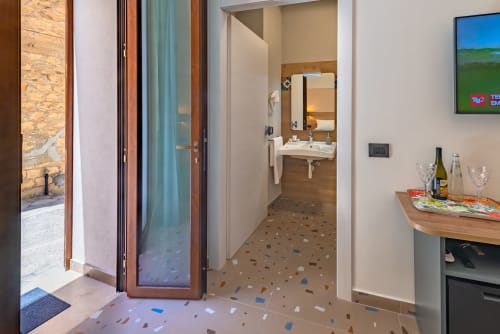 Ingresso della Insolia Room presso Macramè Fazello a Sciacca con bagno, scrivania in legno, TV e pavimentazione in terrazzo