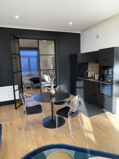 Cuisine ouverte et salle à manger modernes du cottage de Boulogne-sur-Mer avec mobilier noir, table ronde et baies vitrées