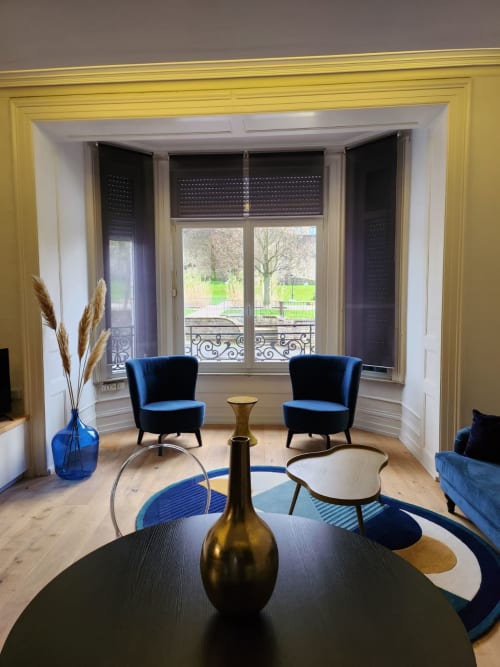 Salon moderne avec fauteuils en velours bleu, table ronde noire et portes-fenêtres donnant sur le parc verdoyant de Boulogne-sur-Mer
